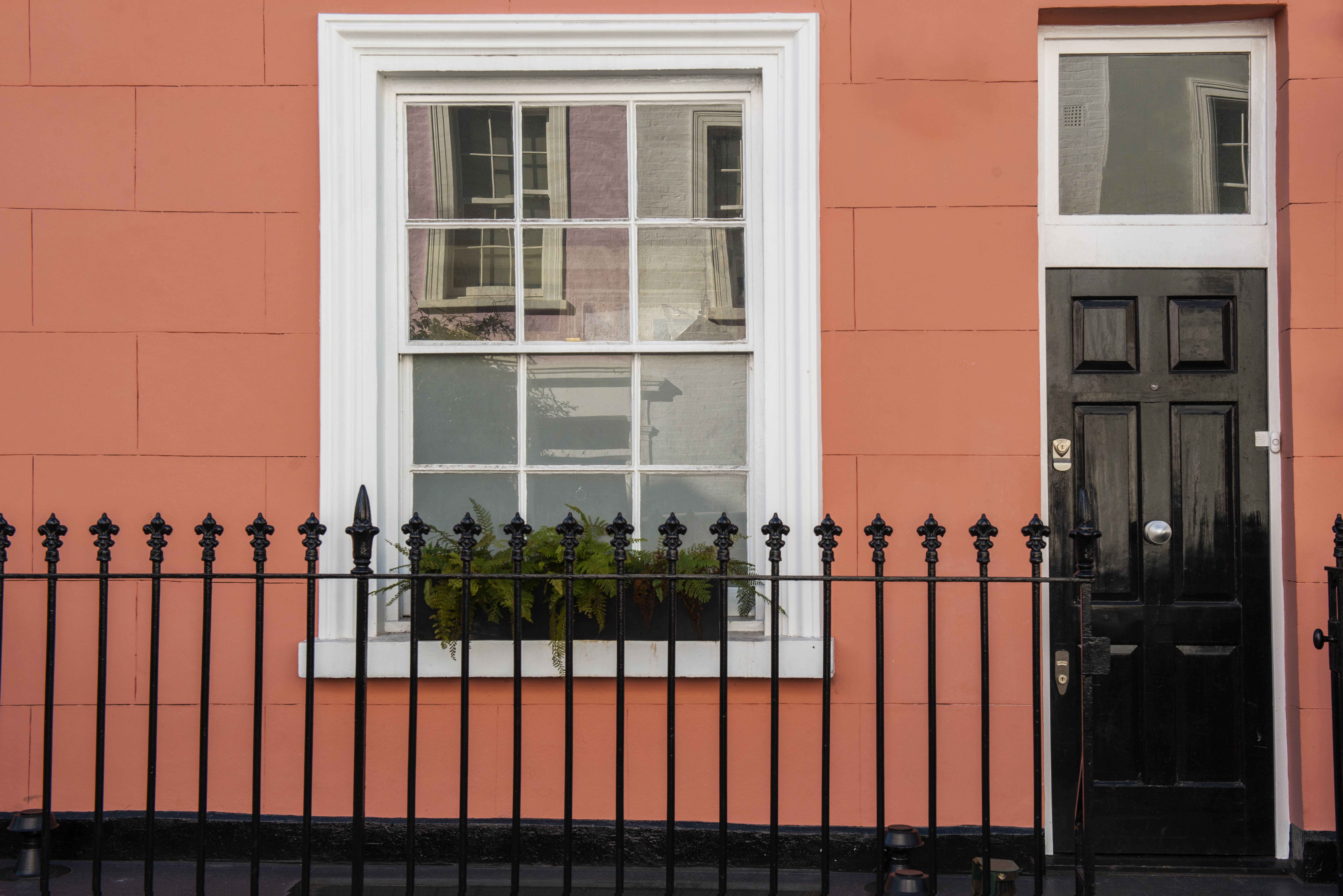 Traditional townhouse featuring a white-framed double-hung window set in a terracotta-colored façade, paired with a black entry door and iron fence