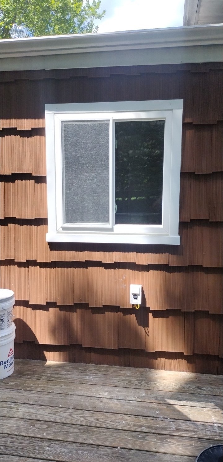 White sliding replacement window installed on a brown cedar-shingle exterior, providing improved ventilation and energy efficiency.